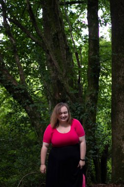 Plus size woman wearing a pink crop top and a black skirt posing in the forest on a travel adventure