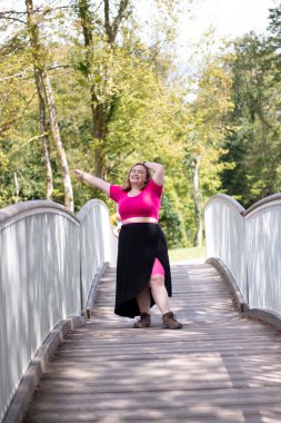 Plus size woman standing on a bridge in Wales wearing a pink crop top and a black skirt