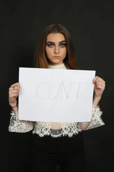 beautiful elegant female holding a sign up that shows the word cunt