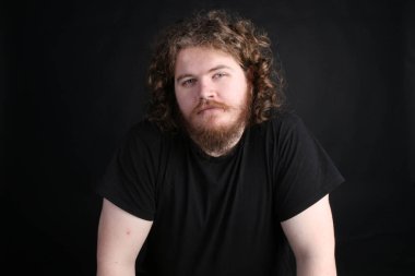 Plus size male with long hair and a beard posing for the camera on a studio backdrop