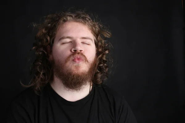 Plus size male with long hair and a beard pulling a funny face on a studio backdrop