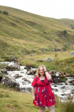 Plus size woman with brunette hair, wearing a red dress while on a travel adventure