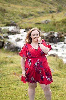 Plus size woman with brunette hair, wearing a red dress while on a travel adventure