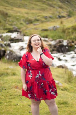 Plus size woman with brunette hair, wearing a red dress while on a travel adventure