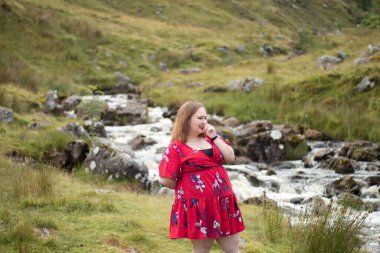 Plus size woman with brunette hair, wearing a red dress while on a travel adventure