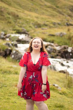 Plus size woman with brunette hair, wearing a red dress while on a travel adventure