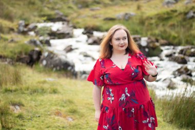 Plus size woman with brunette hair, wearing a red dress while on a travel adventure
