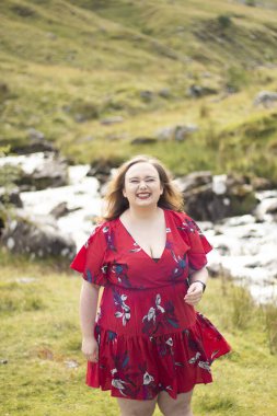 Plus size woman with brunette hair, wearing a red dress while on a travel adventure