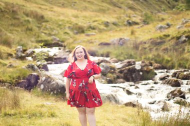 Plus size woman with brunette hair, wearing a red dress while on a travel adventure