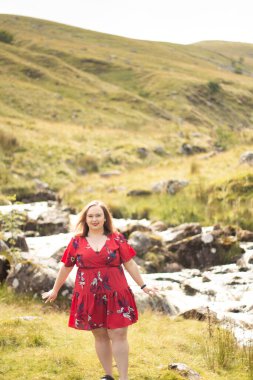 Plus size woman with brunette hair, wearing a red dress while on a travel adventure