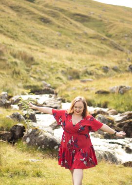 Plus size woman with brunette hair, wearing a red dress while on a travel adventure