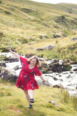 Plus size woman with brunette hair, wearing a red dress while on a travel adventure