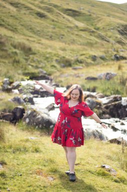 Plus size woman with brunette hair, wearing a red dress while on a travel adventure