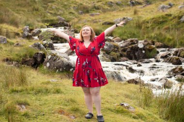 Plus size woman with brunette hair, wearing a red dress while on a travel adventure