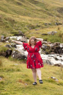 Plus size woman with brunette hair, wearing a red dress while on a travel adventure