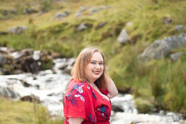 Plus size woman with brunette hair, wearing a red dress while on a travel adventure