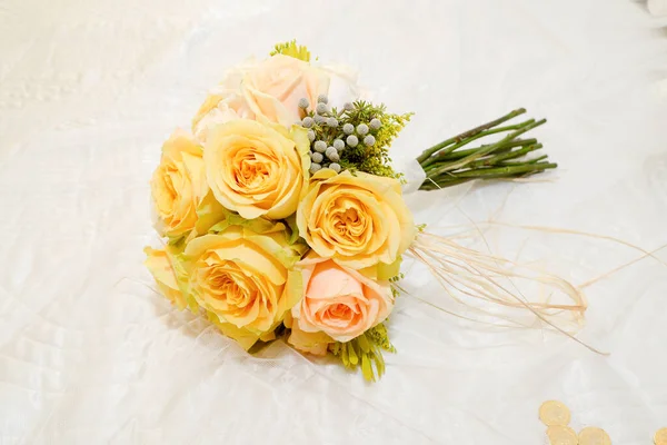 Nice bouquet of yellow roses with a peach colored rose on a white textile background. Bridal bouquet.