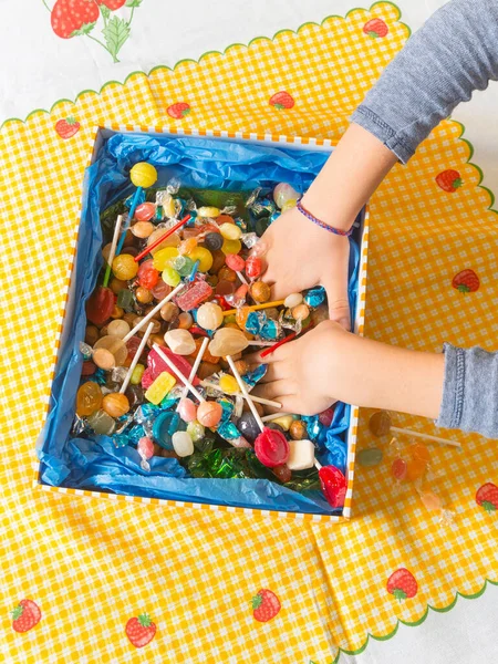 Hands inside a box of sweets. Vertical and top view of the hands of a Caucasian child inside the box catching the candies.