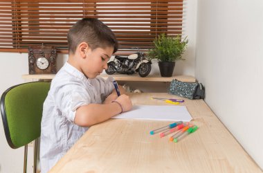Young 8 year old boy writing and drawing on paper inside home.