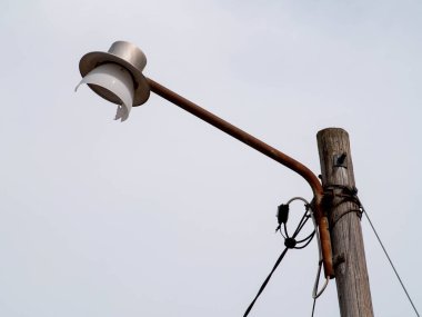 Old rusty destroyed broken street lamp on a rusty metal pole and wooden structure with electric wires