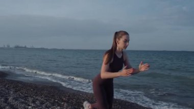 Güzel bir kız plajda spor yapıyor. 4K görüntü. Sahilin arka planında, denizde, dalgalarda, güzel günbatımında ve tepelerde. Güzel gün batımı, ya da gün doğumu. Orta boy..
