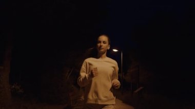 Güzel bir kız gece yolda koşar. Yüksek kalite 4K görüntü. Arka planda lambalar ve ağaçlar var..