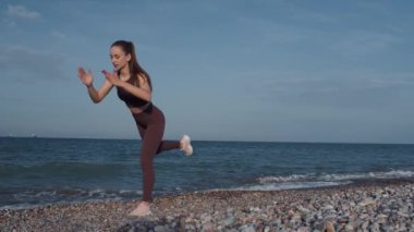 Güzel bir kız plajda spor yapıyor. Yüksek kalite 4K görüntü. Sahilin arka planında, denizde, dalgalarda, güzel günbatımında ve tepelerde. Güzel gün batımı, ya da gün doğumu.