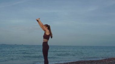 Güzel bir kız plajda spor yapıyor. Yüksek kalite 4K görüntü. Sahilin arka planında, denizde, dalgalarda, güzel günbatımında ve tepelerde. Güzel gün batımı, ya da gün doğumu.