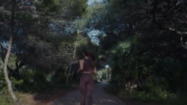 Sportif bir kız spor kıyafetleriyle parkta koşuyor. Ağır çekim. Doğanın, ağaçların ve yolların arka planına karşı. Yüksek kalite 4k görüntü.