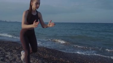 Güzel bir kız plajda spor yapıyor. Yüksek kalite 4K görüntü. Sahilin arka planında, denizde, dalgalarda, güzel günbatımında ve tepelerde. Güzel gün batımı, ya da gün doğumu.