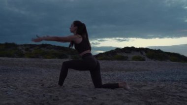 Güzel bir kız plajda spor yapıyor. Yüksek kalite 4K görüntü. Sahilin arka planında, denizde, dalgalarda, güzel günbatımında ve tepelerde. Güzel gün batımı, ya da gün doğumu.