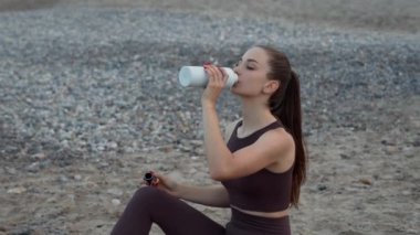 Güzel bir kız sahildeki bir şişe ya da termostan su içer. Denizin arka planında sağlıklı yaşam tarzı ve zindelik. Denizin arka planında sağlıklı yaşam tarzı ve zindelik.