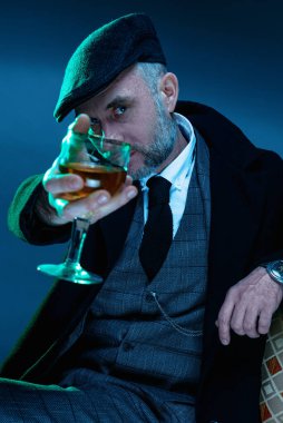 Stüdyoda 40-50 yaşlarında bir iş adamının portresi. Elinde bir bardak tutuyordu. Bu da fotoğrafçıyı gösteriyor. Klasik bir palto ve şapka giymişti..