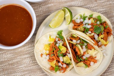 Overhead of tacos al pastor with salsa roja and limes