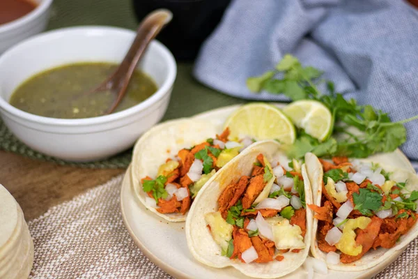 Platter of mexican tacos al pastor with salsa verde and limes