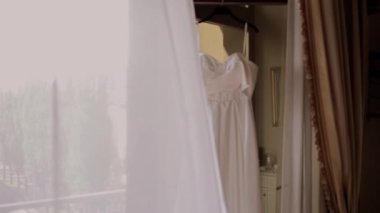 bride's white wedding dress hanging in the room
