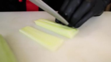 Aşçı mutfakta bıçakla taze salatalık keser.