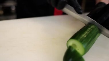 Aşçı mutfakta bıçakla taze salatalık keser.