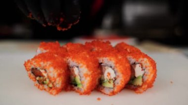 Erkek bir şef Japon suşisini kırmızı tobiko havyarına sarar.