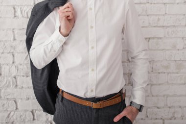 Beyaz gömlekli ve ceketli bir adam tuğla duvarın yanında.