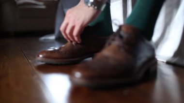 Kahverengi deri ayakkabılara ayakkabı bağlayan bir adam.