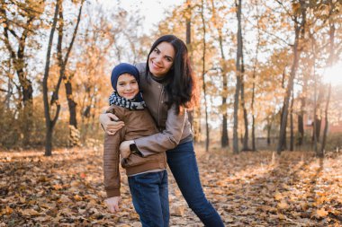 Sonbahar parkında annesinden portakal yapraklı bir oğul.