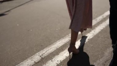 Bir kadınla birlikte bir adam asfaltta yürüyor. Şehir ayaklarında, yakın plan ayakkabılarla.