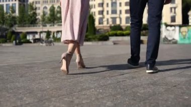 Bir kadınla birlikte bir adam asfaltta yürüyor. Şehir ayaklarında, yakın plan ayakkabılarla.