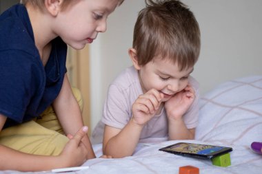 Evde akıllı telefonla oynayan iki anaokulu çocuğu.