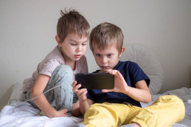 Evde akıllı telefonla oynayan iki anaokulu çocuğu.