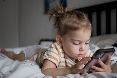 Küçük kız akıllı telefonuyla evde yatağında oynuyordu. Kafkasyalı küçük kız..