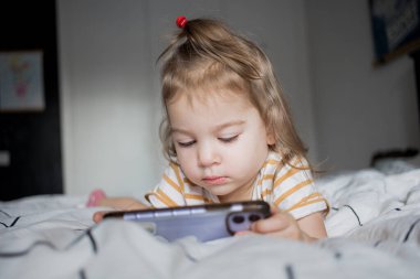 Küçük kız akıllı telefonuyla evde yatağında oynuyordu. Kafkasyalı küçük kız..