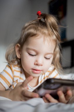 Küçük kız akıllı telefonuyla evde yatağında oynuyordu. Kafkasyalı küçük kız..