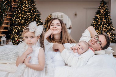 Tarafsız giysiler içinde mutlu beyaz bir aile anne, baba, kız ve oğul yatakta uzanıyorlar. 